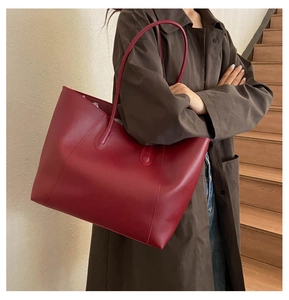 Close-up of a large red leather tote bag with long straps worn on shoulder by a model