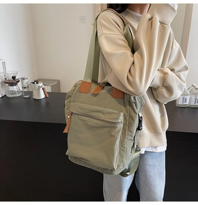 Sage green convertible canvas backpack with leather accents and front zipper pocket detail