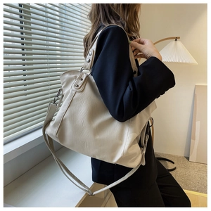 Close-up of a large beige PU leather tote bag featuring metal rivets and wide shoulder strap