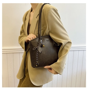 Detail of dark brown leather tote bag with tennis racket charm and woven rope decoration