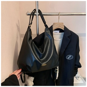 Detail of black textured leather hobo bag with gold handmade plate on metal rack