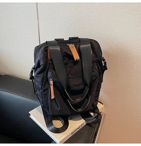 Macro detail of black nylon backpack featuring brown leather zipper pulls and front pocket
