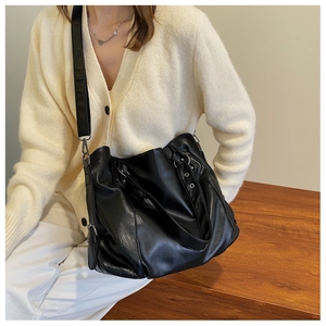 Model wearing a large black soft leather tote bag with side buckle and adjustable strap