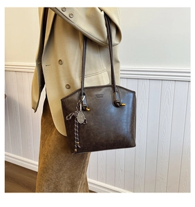 Detailed view of dark brown leather tote bag with knotted straps and decorative metal charm