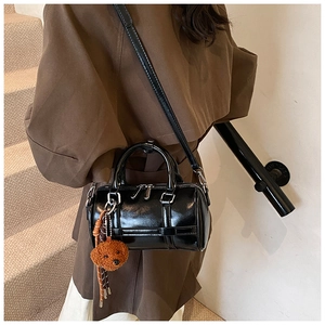 Détail du sac Boston noir brillant avec breloque ours et bandoulière réglable