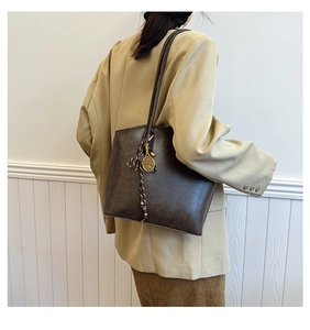 Detail of dark brown vintage tote bag with long shoulder straps and gold tennis racket charm