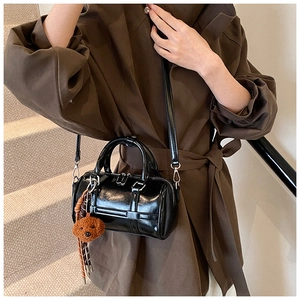 Sac Boston noir verni avec charm d'ours porté par un mannequin en manteau chic