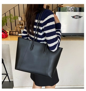Close-up of a large black leather tote bag in a cafe showing smooth texture and double straps