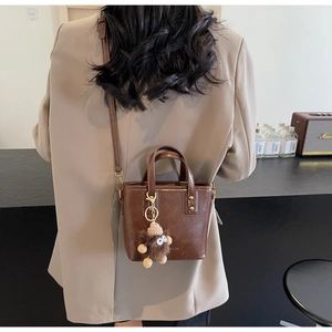Détail du sac seau en cuir marron foncé avec un charmant pendentif monstre en peluche