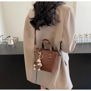 Détail d'un sac cabas vintage marron avec breloque peluche sur un mannequin stylé