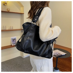 Detail of black faux leather tote bag with wide strap and metallic ring accents