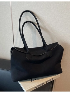 Minimalist black canvas tote bag with long cylindrical straps on a white book base
