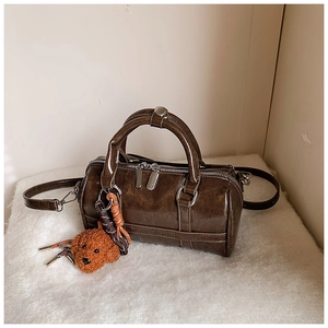 Détail d'un sac Boston marron avec texture cirée et charm ours en peluche sur fourrure blanche