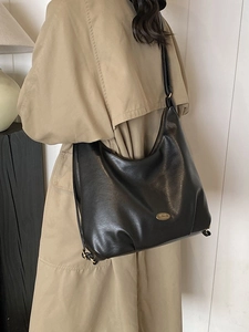 Classic black leather tote bag with gold logo shown on model in khaki trench coat