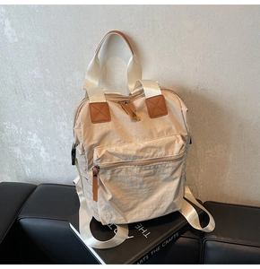 Detailed top-down view of beige nylon backpack with brown leather accents and large front pocket
