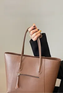 Close-up of brown leather tote bag showing fine stitching and exterior zipper pocket