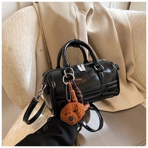 Détail du sac Boston noir brillant avec breloque ours sur fond de blazer beige élégant