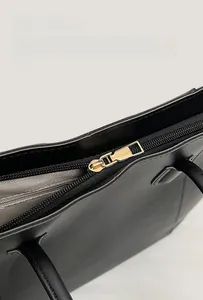 Detailed close-up of smooth gold zipper hardware on black leather tote bag