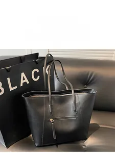 Detailed view of a black minimalist tote bag with smooth texture on a leather sofa
