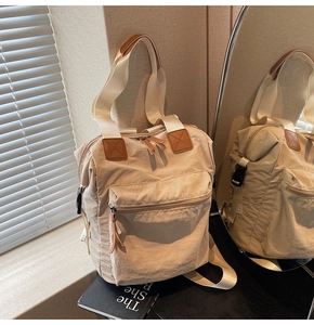 Detail of beige nylon multi-way backpack showing the brown leather patch and side buckle strap