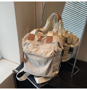 Detail of off-white nylon backpack showing textured fabric and brown leather zipper pulls
