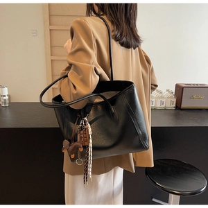Detailed view of black oversized leather tote bag styled with charms on a female shoulder