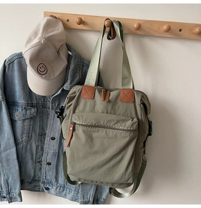 Detail of army green nylon backpack showing large front zipper pocket and leather handles