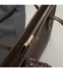 Detail of smooth gold-tone zipper and lychee texture on brown leather tote bag