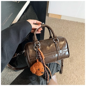Détail du sac Boston marron foncé avec breloque ours en peluche et pompons tissés