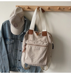 Detail of beige canvas tote bag with brown leather zipper pulls and front pocket