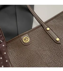 Close-up of brown litchi leather tote with golden DA logo and polka dot silk scarf
