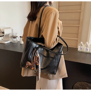 Close-up of a large black leather tote bag with creative dog charm and braided detail
