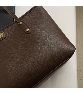 Close-up of deep brown tote bag with litchi grain texture and gold metal rivet details