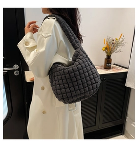 Detail of a dark grey quilted bucket bag shown on a model in a minimalist urban setting