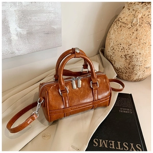 Sac Boston vintage marron en cuir avec détails argentés posé sur un trench-coat beige