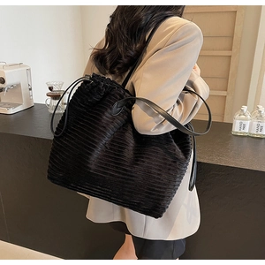 Detail of black corduroy tote bag with leather strap worn by model in minimalist cafe