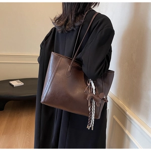 Close-up of a large coffee brown tote bag with dog pendant and woven fringe detail