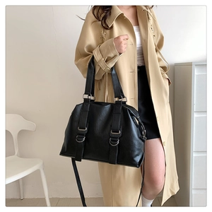 Detailed view of black leather tote bag with silver hardware on beige trench coat