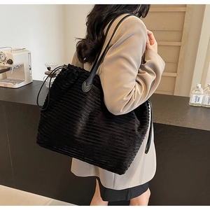 Side view of black corduroy tote bag with drawstring closure and slim leather shoulder straps