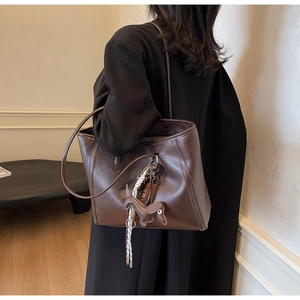 Detailed view of deep brown faux leather tote bag with stitch details and charm on black coat