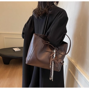 Detail of a dark brown leather tote bag featuring a cute dog charm and woven tassels