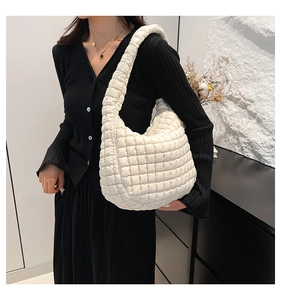 Detailed view of cream quilted hobo shoulder bag with puffy texture on black outfit