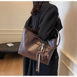 Detail of dark brown leather tote bag with puppy charm and woven tassel detail