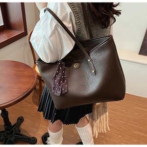 Detailed macro view of dark brown lychee textured leather tote bag with silk scarf charm