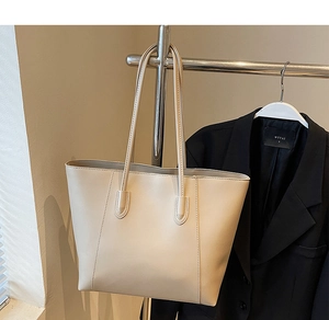 Detail of off-white tote bag hanging on a metal rack with sleek matte leather texture