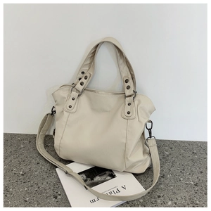 Detail of a cream faux leather tote bag with vintage metal rivets and adjustable strap