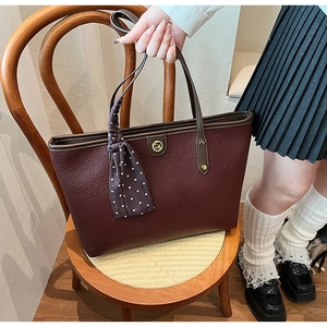 Close-up of burgundy tote bag with gold logo, pebbled texture and silk scarf detail