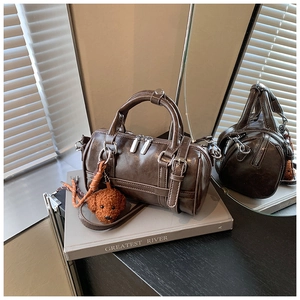 Détail d'un sac Boston marron avec texture en PU, double fermeture éclair et charm d'ours en peluche