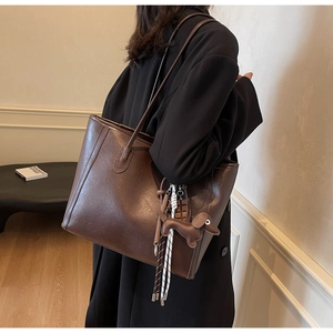 Detail of dark brown leather tote bag with dog charm and woven tassel decoration