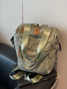 Olive green nylon backpack with top handle and leather zipper pulls on a leather sofa